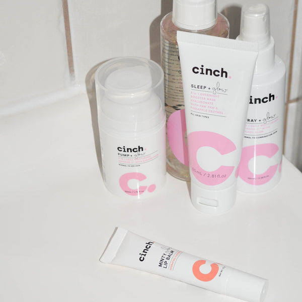 The Everything Set skincare products displayed on a bathroom sink, featuring Cleanse + Glow, Pump + Glow, Spray + Glow, Sleep + Glow, and Minty Glow Lip Balm. A complete day and night skincare routine for all skin types, focusing on hydration, plumping, and glowing skin.